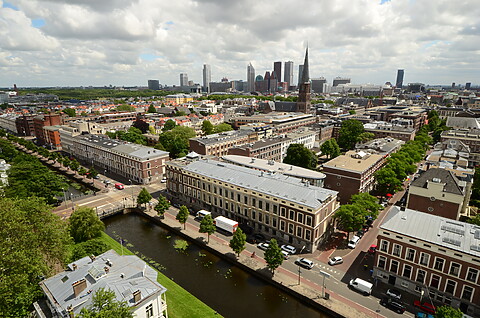 Uitzicht over Den Haag. Met op de voorgrond een gracht, daarachter blokken met huizen en in de verte de skyline met hoge torens