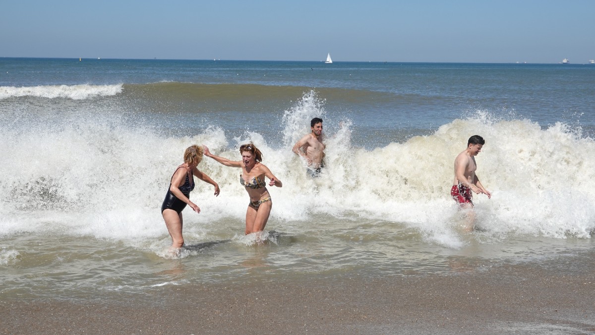 Diverse badgasten genieten bij het Zuiderstrand van hoog opspattende golven in de branding