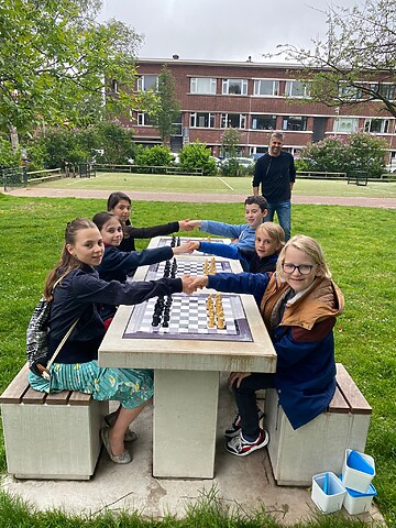 6 jonge kinderen schaken in een park in Segbroek. Ze schudden elkaar sportief de hand voor de wedstrijd.