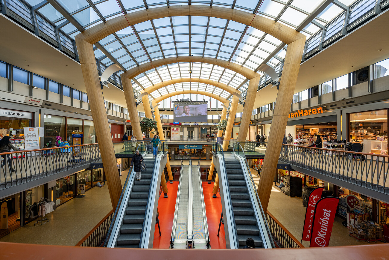 Binnenkant van het winkelcentrum Leyweg. Met houten bogen, roltrappen en verschillende winkels, waaronder VanHaren en Kruidvat.