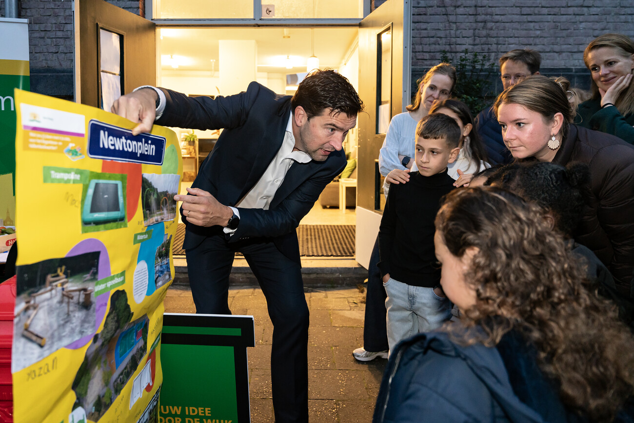 Wethouder Robert van Asten kijkt met kinderen naar een poster met plannen voor het Newtonplein.