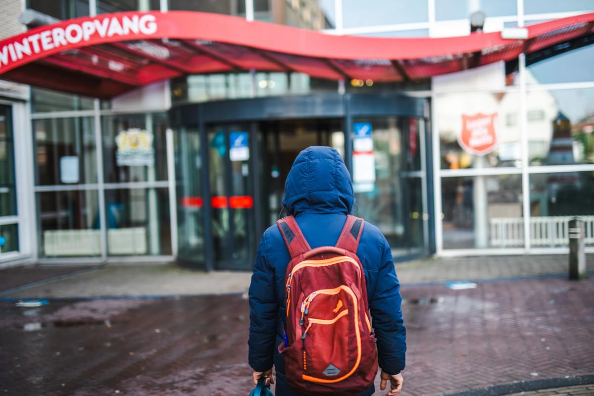 Een persoon met een rugzak loopt richting de winteropvang aan Locatie Sportlaan.