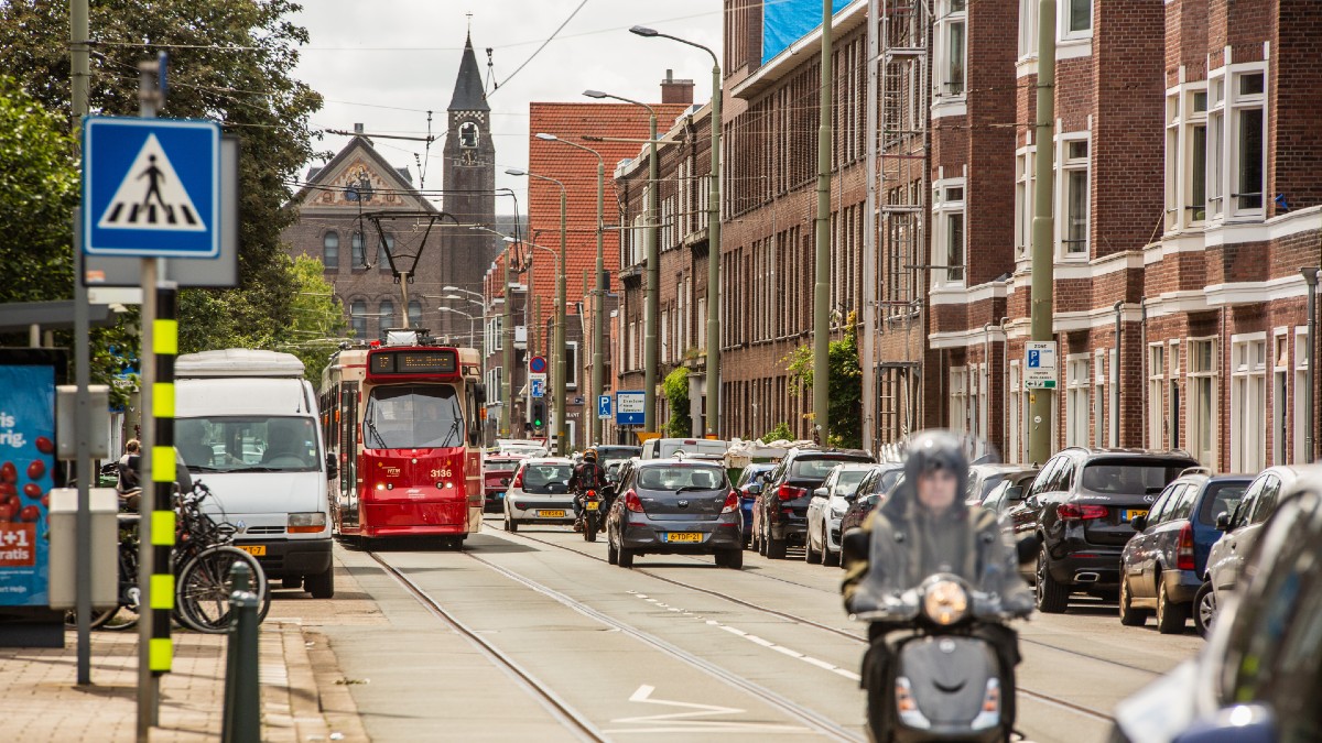 Een levendige Goudenregenstraat met een rijdende tram, scooter en auto's.