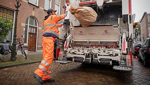 Vuilnisman gooit zak in vuilniswagen