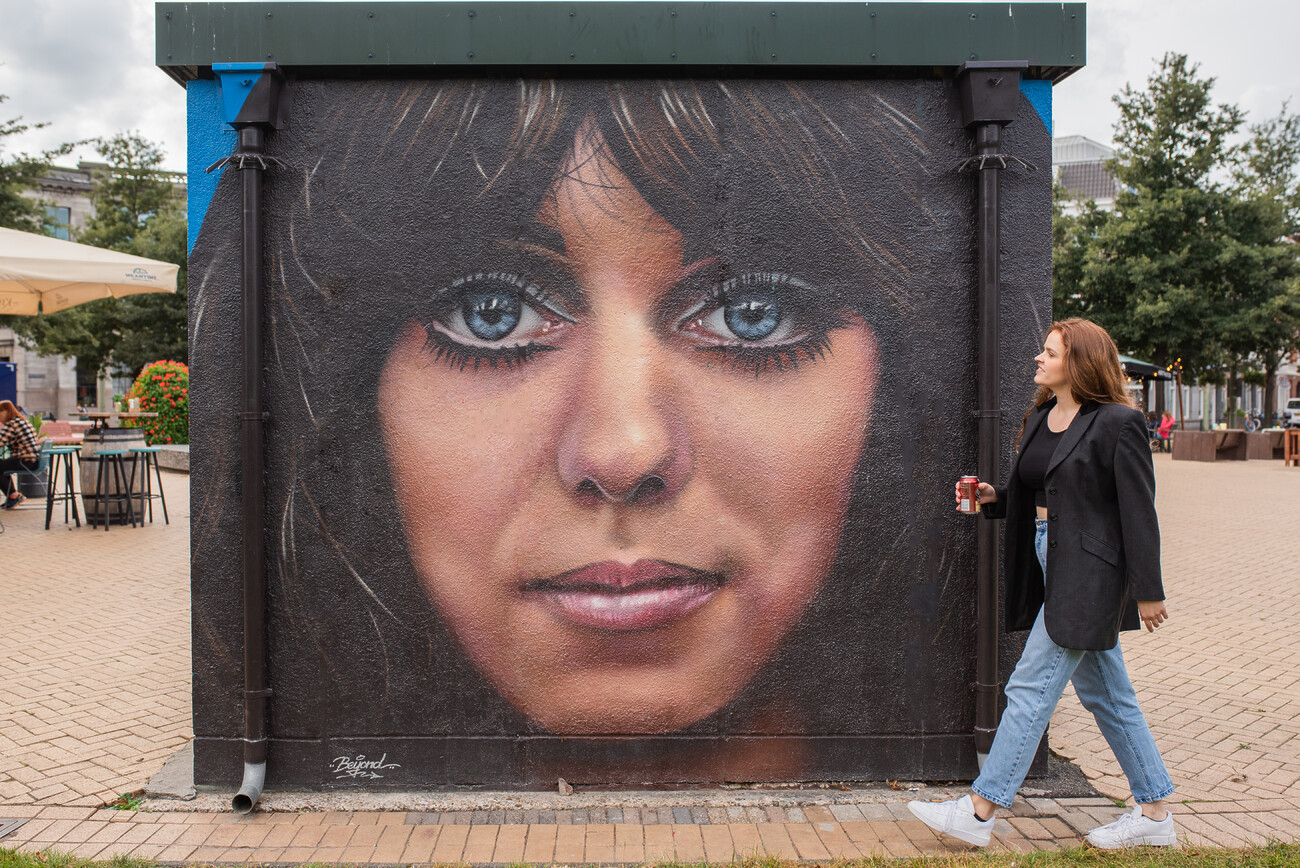 vrouw loopt langs een transformatorhuisje met street art